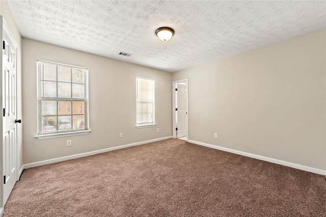 carpeted empty room featuring visible vents, a textured ceiling, and baseboards