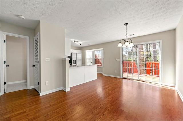 unfurnished living room featuring a notable chandelier, visible vents, a textured ceiling, wood finished floors, and baseboards