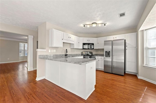 kitchen with stainless steel appliances, visible vents, white cabinets, a sink, and a peninsula