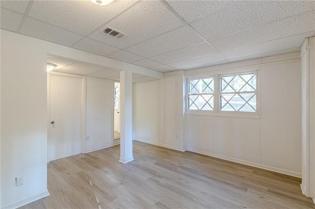 basement with light wood-type flooring and a paneled ceiling