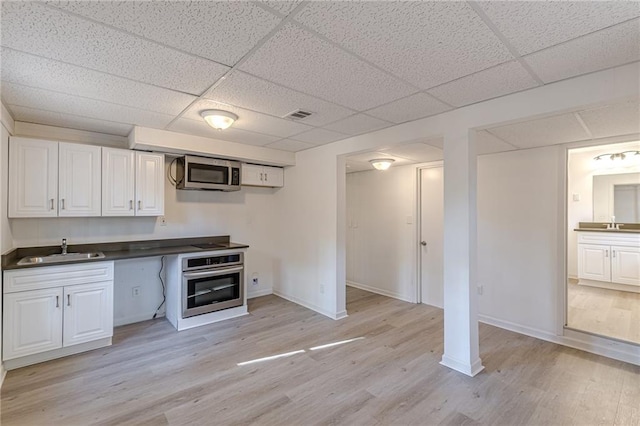 kitchen featuring a paneled ceiling, white cabinets, sink, appliances with stainless steel finishes, and light hardwood / wood-style floors