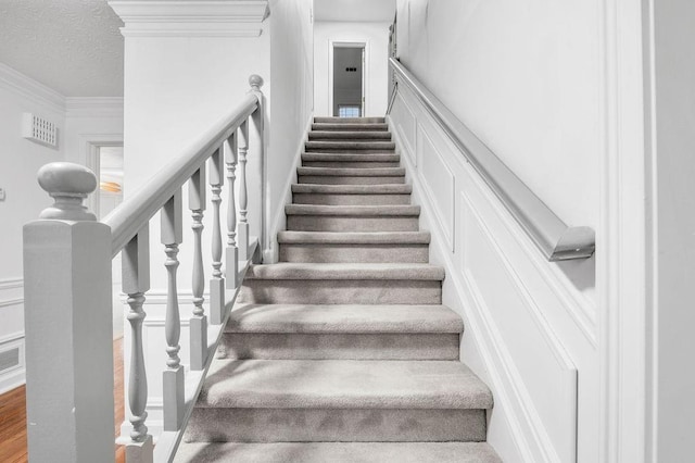 staircase featuring ornamental molding and a textured ceiling