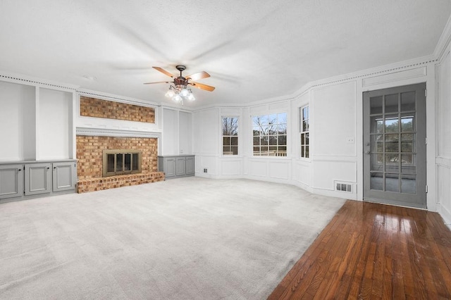 unfurnished living room with a fireplace, carpet floors, ceiling fan, crown molding, and a textured ceiling