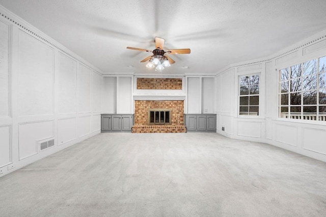 unfurnished living room with a textured ceiling, a fireplace, light colored carpet, and ceiling fan