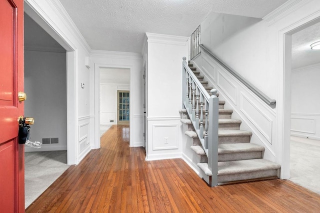 stairway with crown molding, wood-type flooring, and a textured ceiling