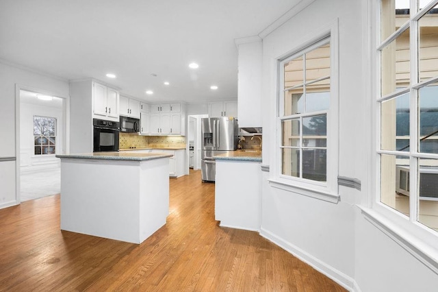 kitchen featuring crown molding, black appliances, light wood-type flooring, white cabinets, and backsplash