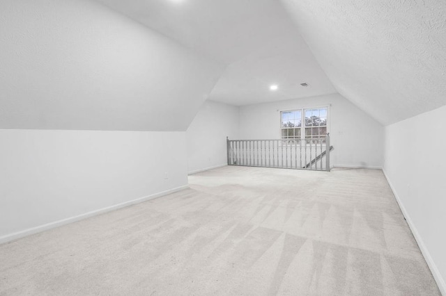 additional living space featuring light carpet, vaulted ceiling, and a textured ceiling