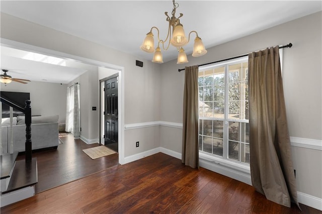 unfurnished dining area featuring ceiling fan with notable chandelier, baseboards, and hardwood / wood-style flooring