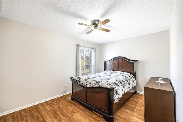 bedroom with ceiling fan, a textured ceiling, baseboards, and wood finished floors