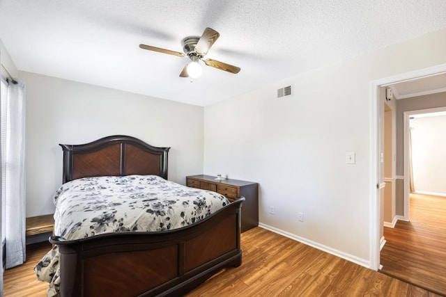 bedroom with a textured ceiling, ceiling fan, wood finished floors, visible vents, and baseboards