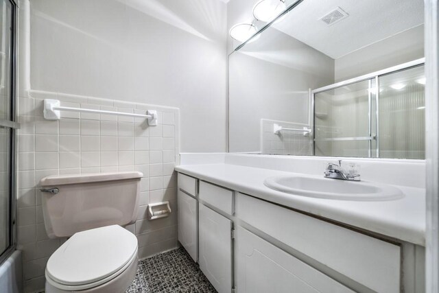 full bathroom with tile walls, visible vents, toilet, a shower with shower door, and vanity