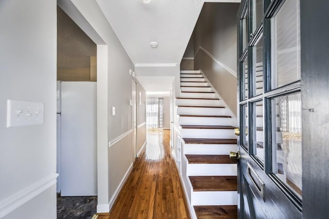 interior space with a textured ceiling, wood finished floors, baseboards, stairs, and ornamental molding