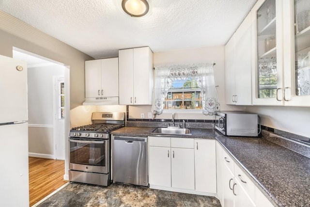 kitchen featuring stainless steel appliances, dark countertops, white cabinets, a sink, and under cabinet range hood