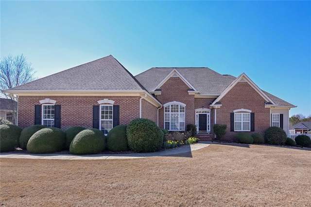 view of front facade featuring brick siding, a front yard, and a shingled roof