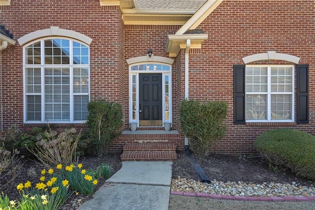 view of exterior entry with brick siding and a shingled roof