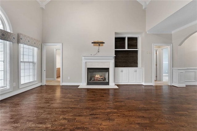 unfurnished living room with dark wood-style floors, a warm lit fireplace, a towering ceiling, and crown molding