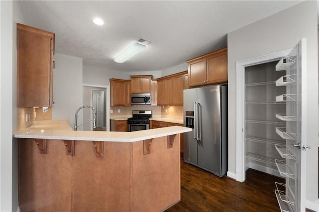 kitchen featuring stainless steel appliances, a peninsula, light countertops, and a kitchen bar