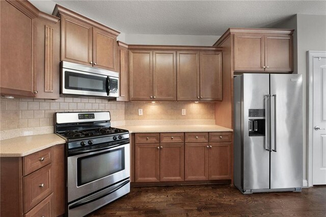 kitchen featuring a textured ceiling, appliances with stainless steel finishes, tasteful backsplash, brown cabinetry, and dark wood finished floors