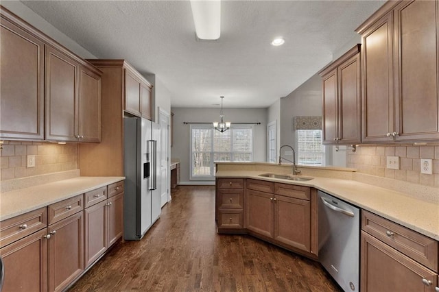 kitchen with decorative light fixtures, stainless steel appliances, light countertops, dark wood-type flooring, and a sink