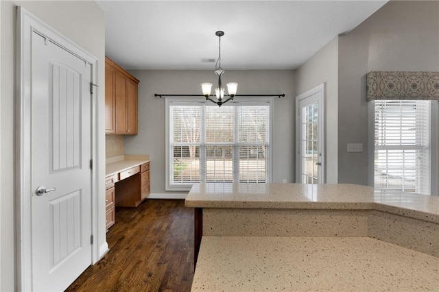 kitchen featuring light stone counters, dark wood finished floors, hanging light fixtures, built in study area, and a chandelier