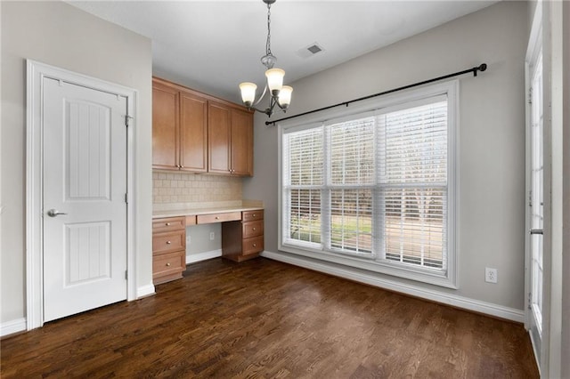 unfurnished office with dark wood-style flooring, visible vents, baseboards, built in desk, and an inviting chandelier