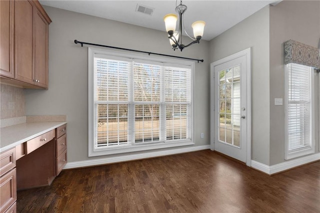 unfurnished dining area featuring a notable chandelier, dark wood-type flooring, visible vents, baseboards, and built in desk