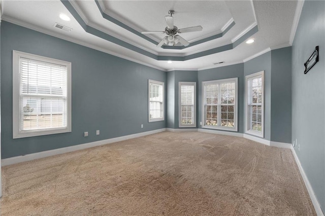 spare room featuring light colored carpet, visible vents, baseboards, a raised ceiling, and crown molding