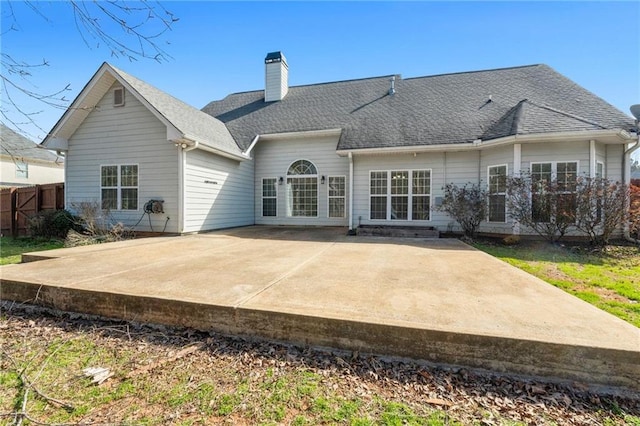 back of property with a patio, a shingled roof, a chimney, and fence