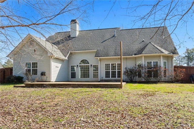 rear view of house with a yard, a chimney, and fence