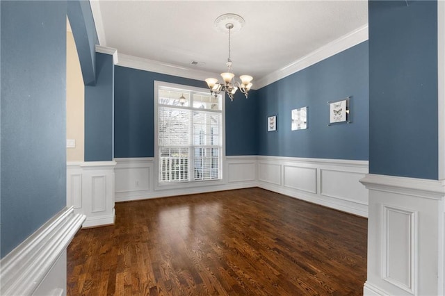 unfurnished dining area featuring a wainscoted wall, ornamental molding, dark wood finished floors, and a notable chandelier