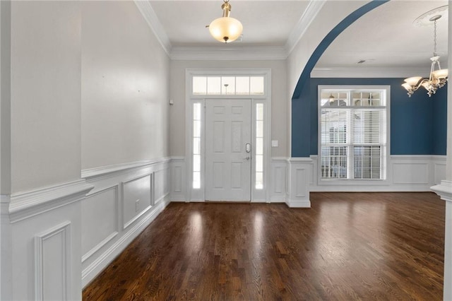 entrance foyer featuring arched walkways, ornamental molding, wainscoting, dark wood-style floors, and an inviting chandelier