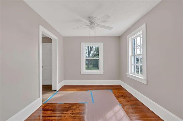 unfurnished room featuring a ceiling fan, baseboards, a wealth of natural light, and wood finished floors