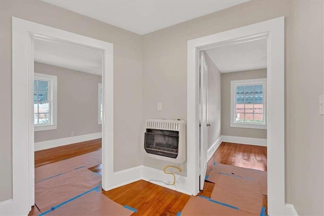 corridor with baseboards, wood finished floors, and heating unit