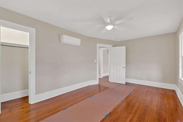 unfurnished bedroom featuring a closet, wood-type flooring, a wall mounted AC, a ceiling fan, and baseboards