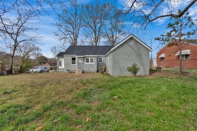 back of house featuring entry steps, a lawn, and fence