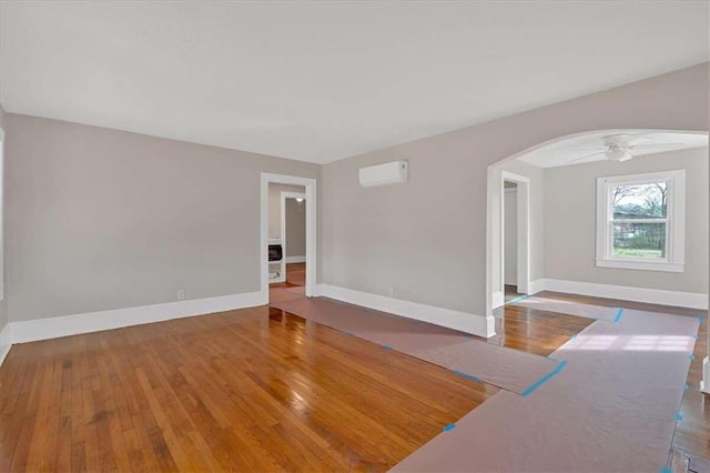 spare room with baseboards, arched walkways, a ceiling fan, hardwood / wood-style flooring, and an AC wall unit