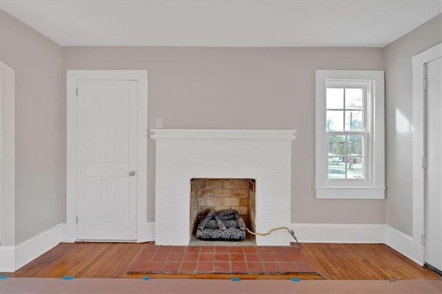 unfurnished living room featuring a brick fireplace, baseboards, and wood finished floors