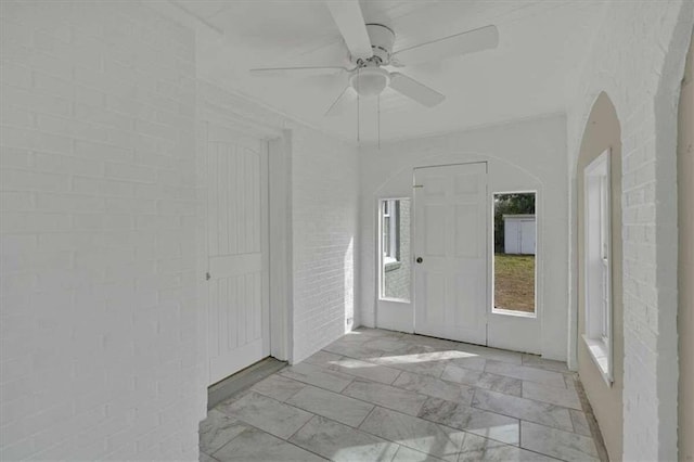 entryway featuring ceiling fan and brick wall