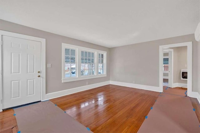 foyer entrance featuring heating unit, baseboards, wood finished floors, and a glass covered fireplace