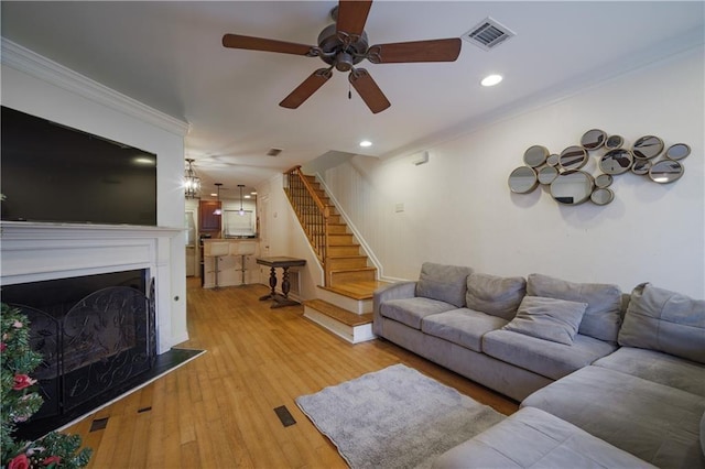 living room with light wood finished floors, visible vents, ornamental molding, stairs, and a fireplace