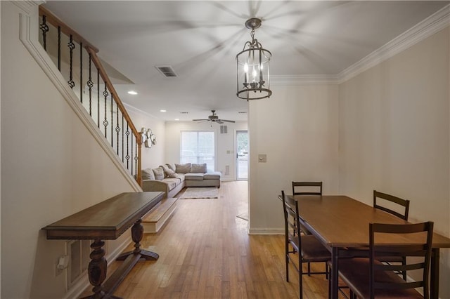 dining space featuring visible vents, baseboards, stairway, light wood finished floors, and crown molding