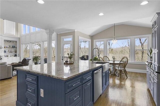 kitchen with wood finished floors, blue cabinetry, a kitchen island with sink, a sink, and vaulted ceiling