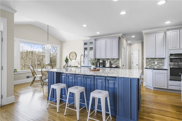 kitchen with light wood-style flooring, an island with sink, vaulted ceiling, double oven, and a kitchen breakfast bar