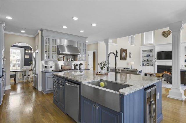 kitchen featuring wine cooler, stainless steel appliances, wall chimney range hood, and decorative columns