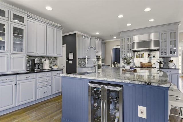 kitchen with beverage cooler, wood finished floors, arched walkways, crown molding, and a large island with sink