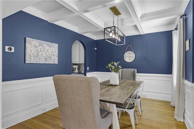 dining space with a wainscoted wall, beam ceiling, light wood-style floors, arched walkways, and a notable chandelier