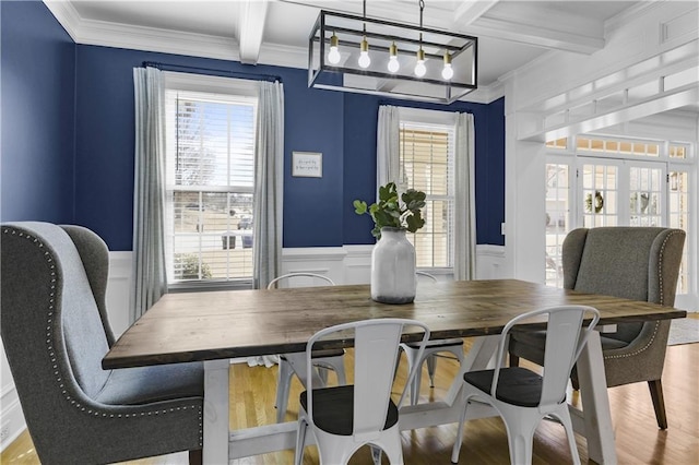 dining room featuring beamed ceiling, wood finished floors, wainscoting, and crown molding