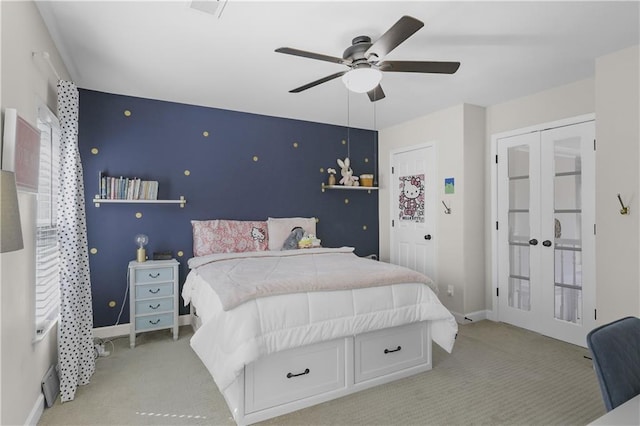 carpeted bedroom featuring an accent wall, french doors, baseboards, and ceiling fan