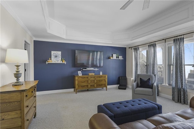 carpeted living room with a raised ceiling, a ceiling fan, baseboards, and ornamental molding