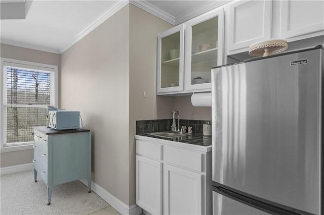 kitchen featuring white microwave, glass insert cabinets, crown molding, freestanding refrigerator, and white cabinetry